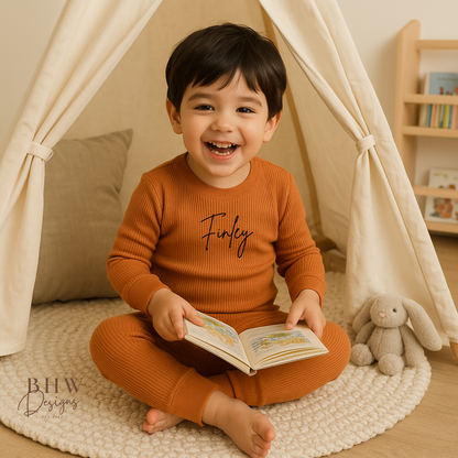 Child in a rust outfit with 'Finley' printed on it, sitting inside a teepee reading a book.