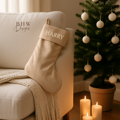 Beige Christmas stocking with 'HARRY' on a beige armchair next to a decorated Christmas tree.