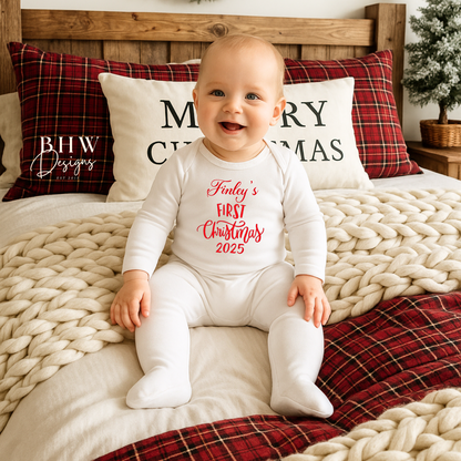 Baby wearing a 'Finley's First Christmas' onesie sitting on a bed with festive pillows and decorations.
