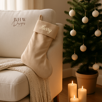 Beige Christmas stocking with 'Harry' on a beige armchair next to a decorated Christmas tree.