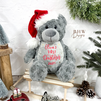 Grey teddy bear with a red Santa hat and 'Olivia's First Christmas 2025' on the front.