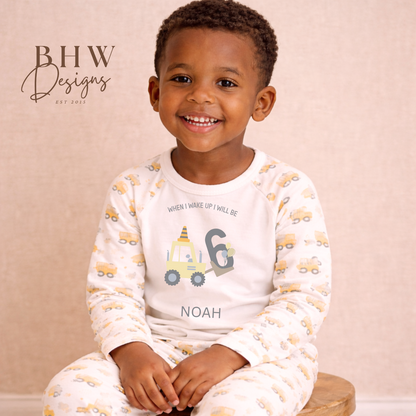 Child wearing pyjamas with a digger pattern and 'Noah' printed on them, sitting on a wooden stool