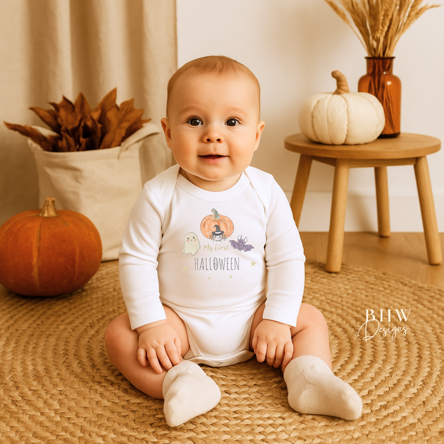 Baby wearing a My First Halloween onesie sitting on a woven mat with pumpkins in the background.
