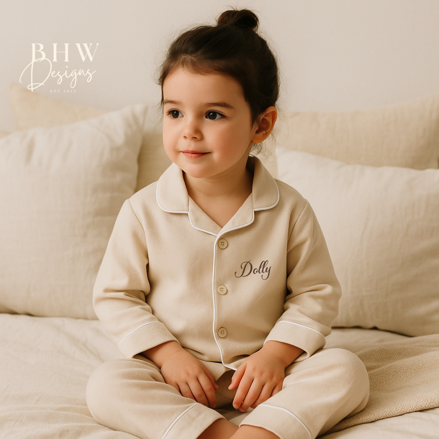 Child wearing a cotton beige pyjama set with 'Dolly' printed on it, sitting on a beige couch.