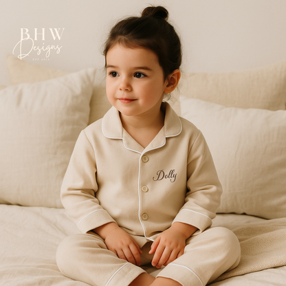 Child wearing a cotton beige pyjama set with 'Dolly' printed on it, sitting on a beige couch.