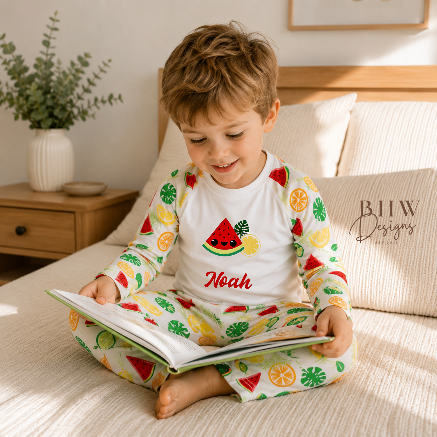 Child wearing a colourful pyjamas with fruit patterns, sitting on a bed reading a book.
