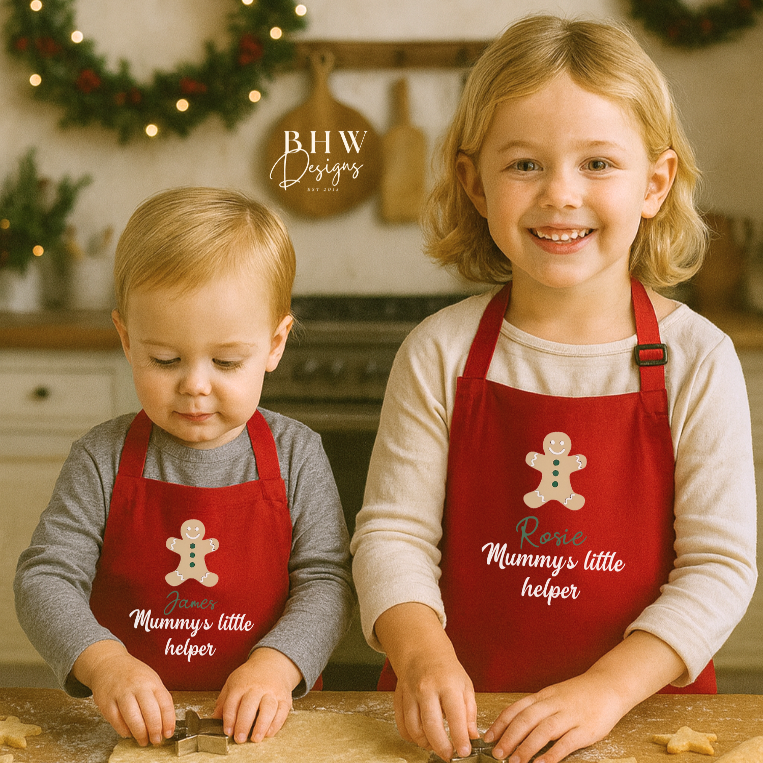 Two children wearing personalised red aprons with gingerbread men designs in a kitchen setting.