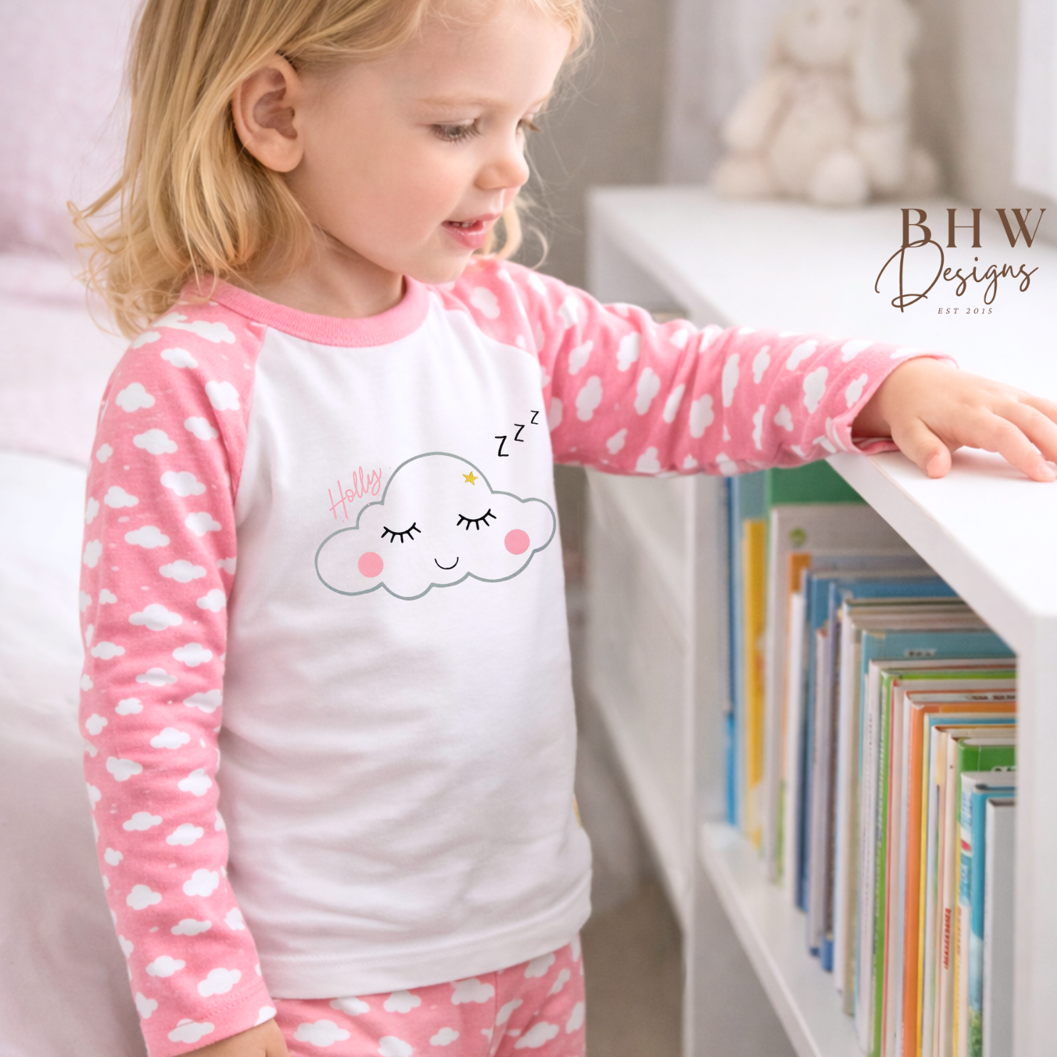 Child wearing a pink and white cloud-themed pajama set, standing next to a bookshelf.