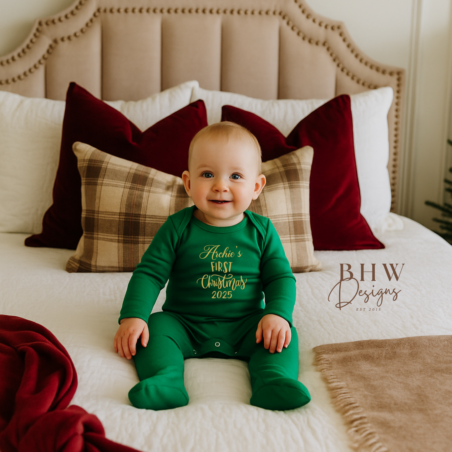 Baby in a green onesie with Archies's First Christmas 2025 On the front in Gold