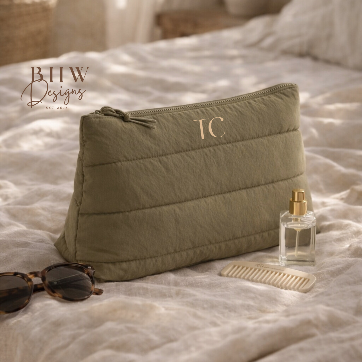 Green quilted pouch with initials on a bed with sunglasses and perfume bottle