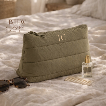 Green quilted pouch with initials on a bed with sunglasses and perfume bottle