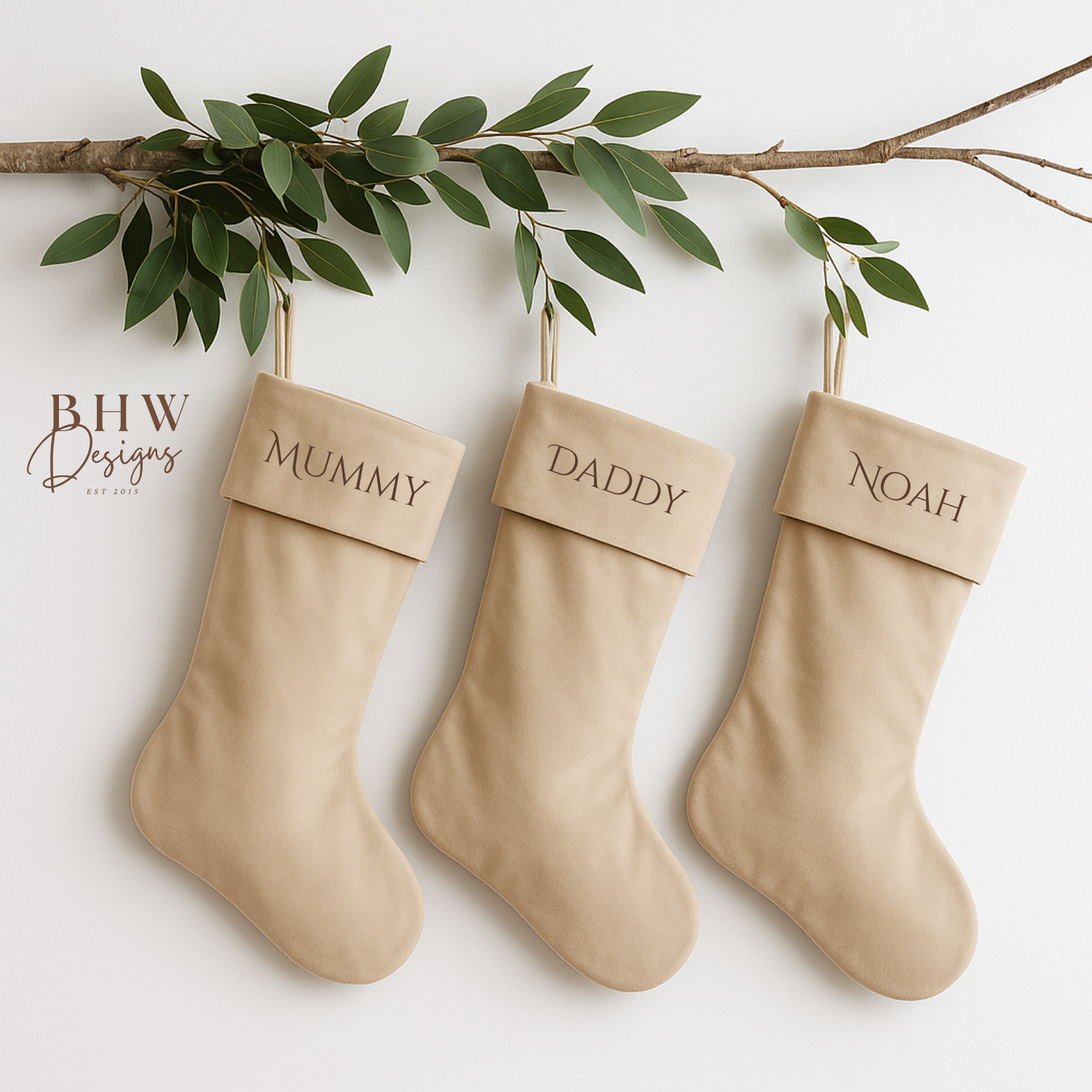 Three beige stockings labeled 'Mummy', 'Daddy', and 'Noah' hanging on a branch with green leaves.