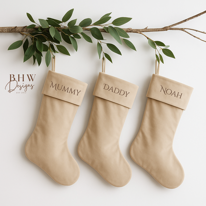 Three beige stockings labeled 'Mummy', 'Daddy', and 'Noah' hanging on a branch with green leaves.