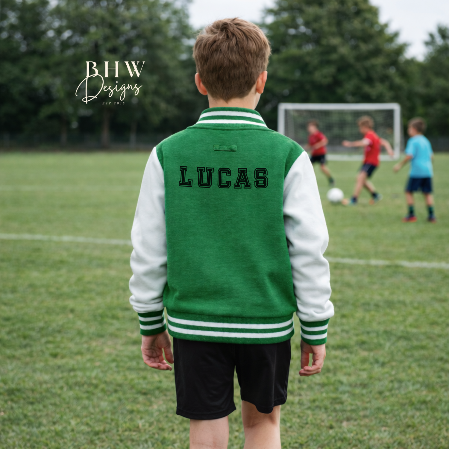 Child wearing a green and white letterman jacket with 'LUCAS' on a soccer field.