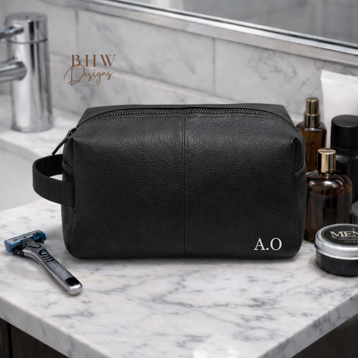 Black leather toiletry bag on a marble bathroom counter with grooming products.