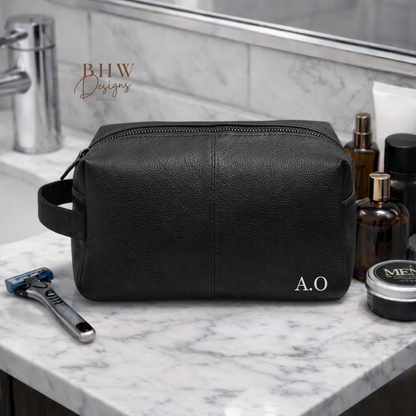 Black leather toiletry bag on a marble bathroom counter with grooming products.