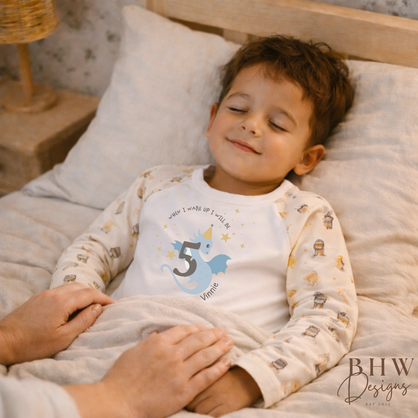 Child in pajamas with a birthday design lying on a bed, holding a hand.