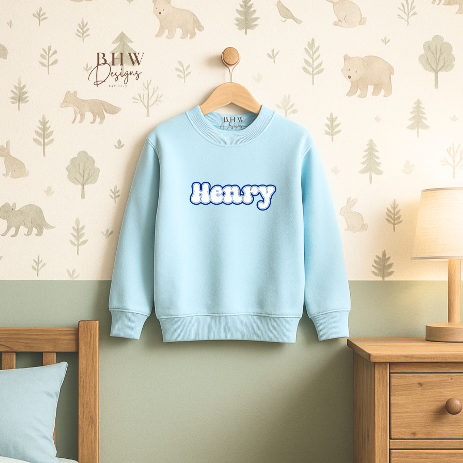 Light blue sweatshirt with 'Henry' printed on it hanging on a wooden hanger against a wall with animal prints.