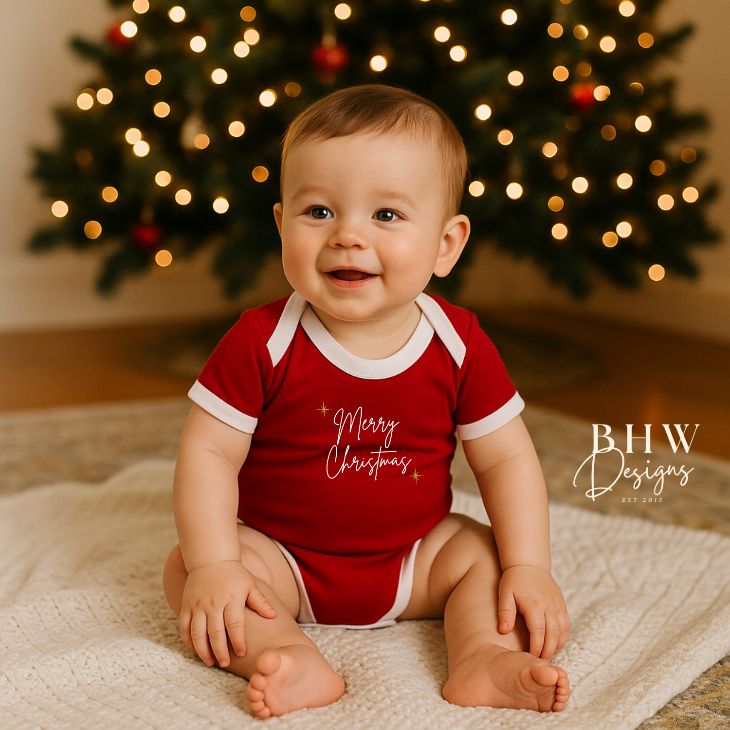 Baby wearing a red 'Merry Christmas' onesie in front of a decorated Christmas tree.