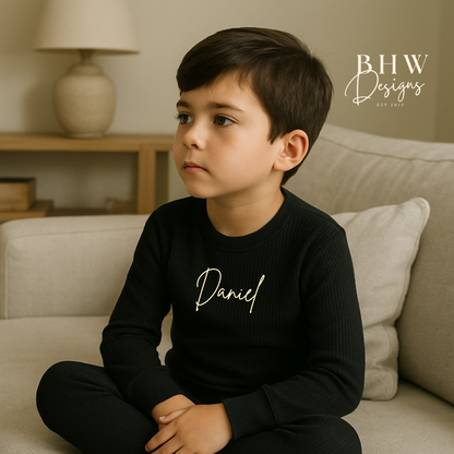 Child wearing a ribbed black outfit with 'Daniel' printed on it, sitting on a couch in a home setting.