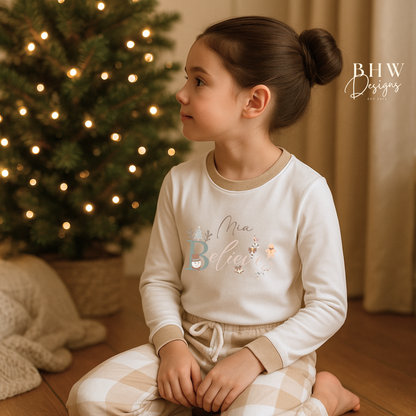 Child wearing a white long-sleeve top with beige cuffs personalised on the front with believes and beige and white check trousers