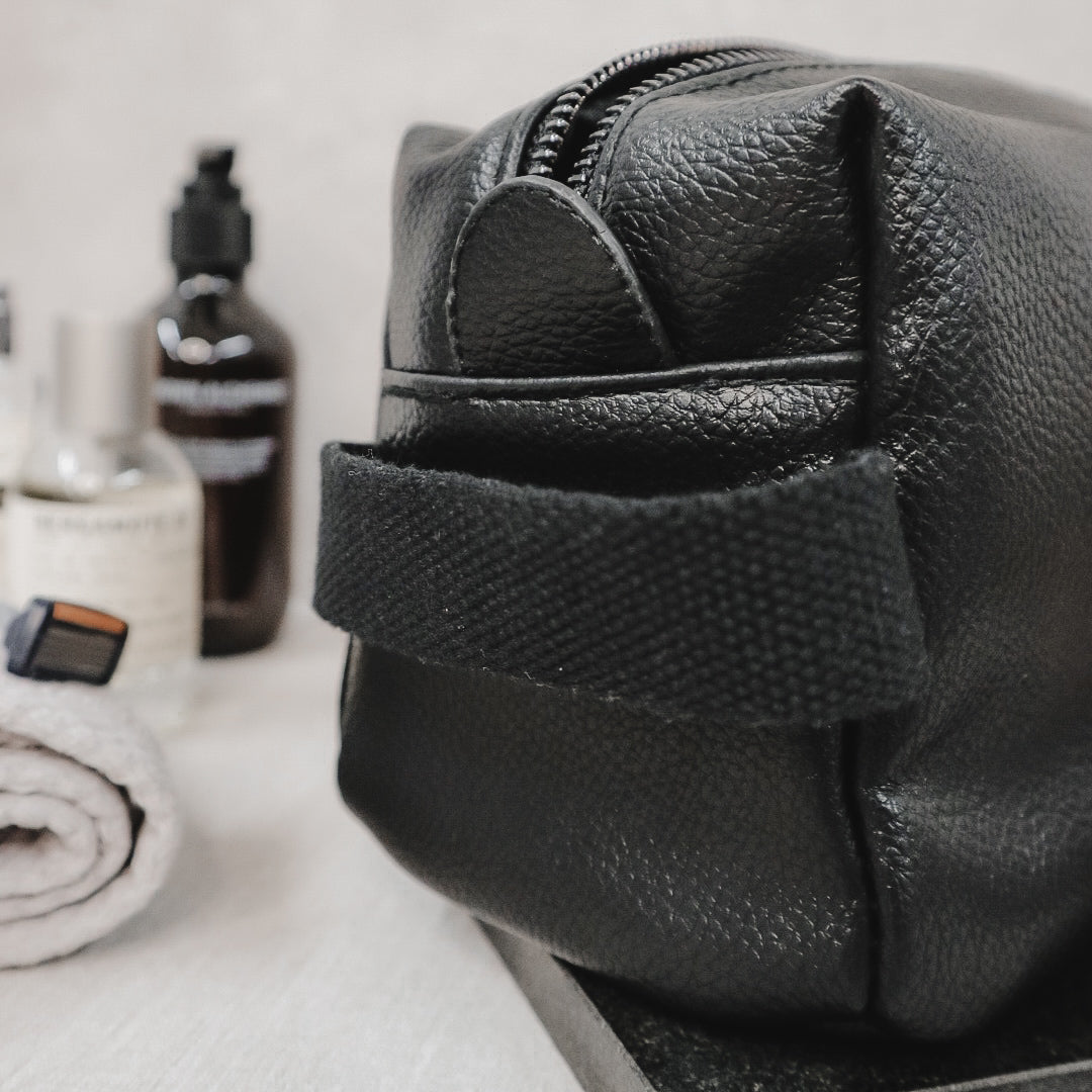 Black leather dopp kit with grooming products on a white surface