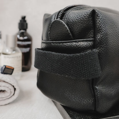 Black leather dopp kit with grooming products on a white surface