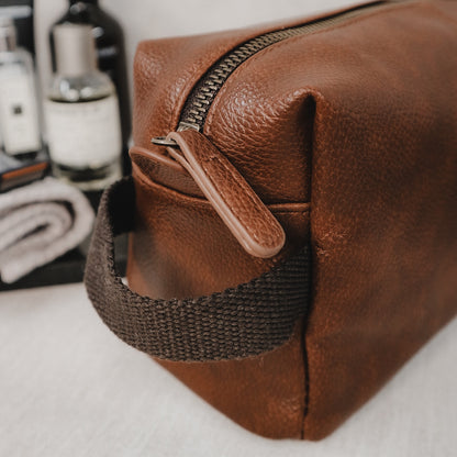 Brown faux leather toiletry bag with a strap on a white surface