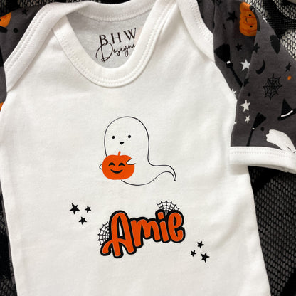 White baby onesie with ghost and pumpkin design, featuring the name 'Amie', on a black and gray patterned background.