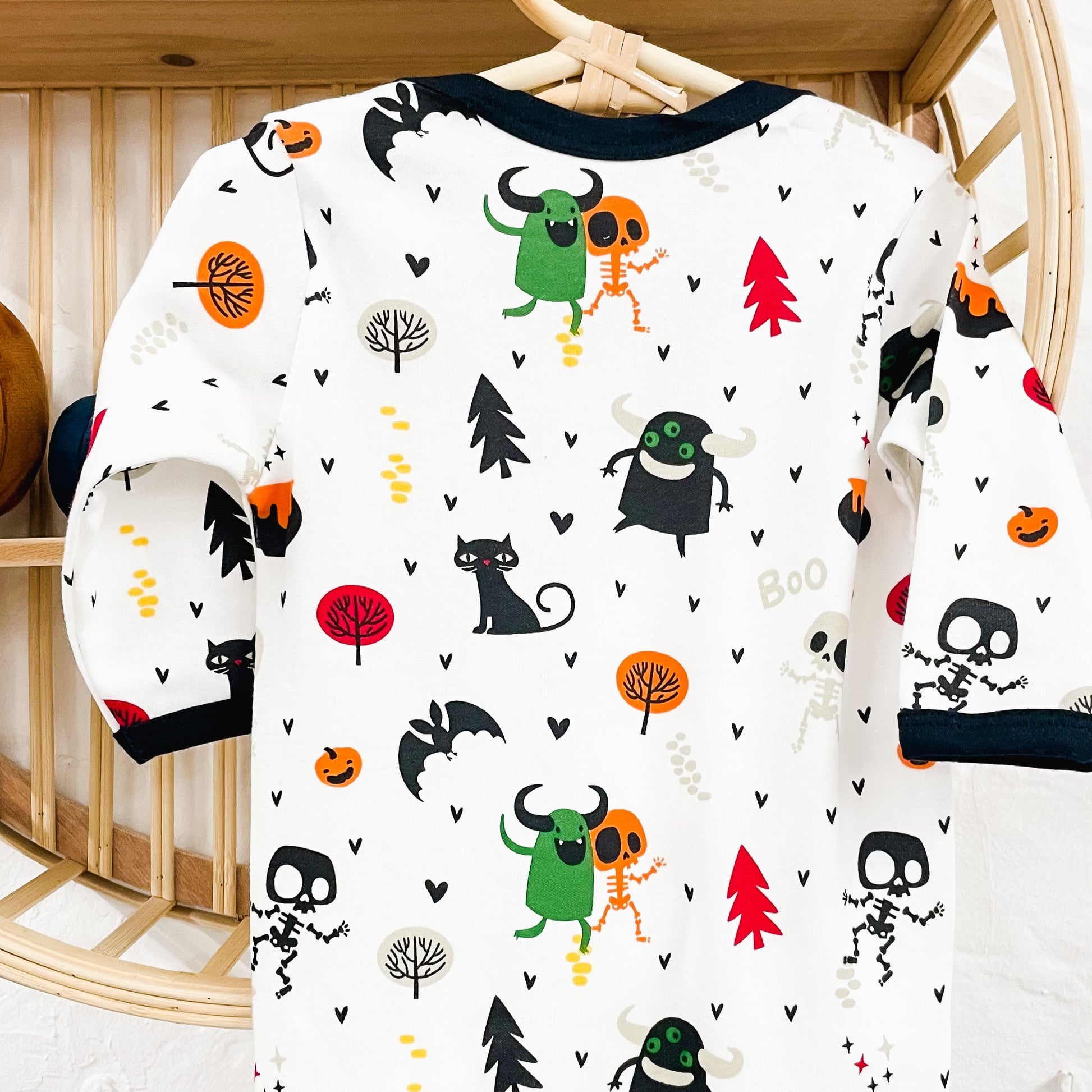 Long-sleeve bodysuit with Halloween-themed pattern on a hanger against a wooden shelf background.