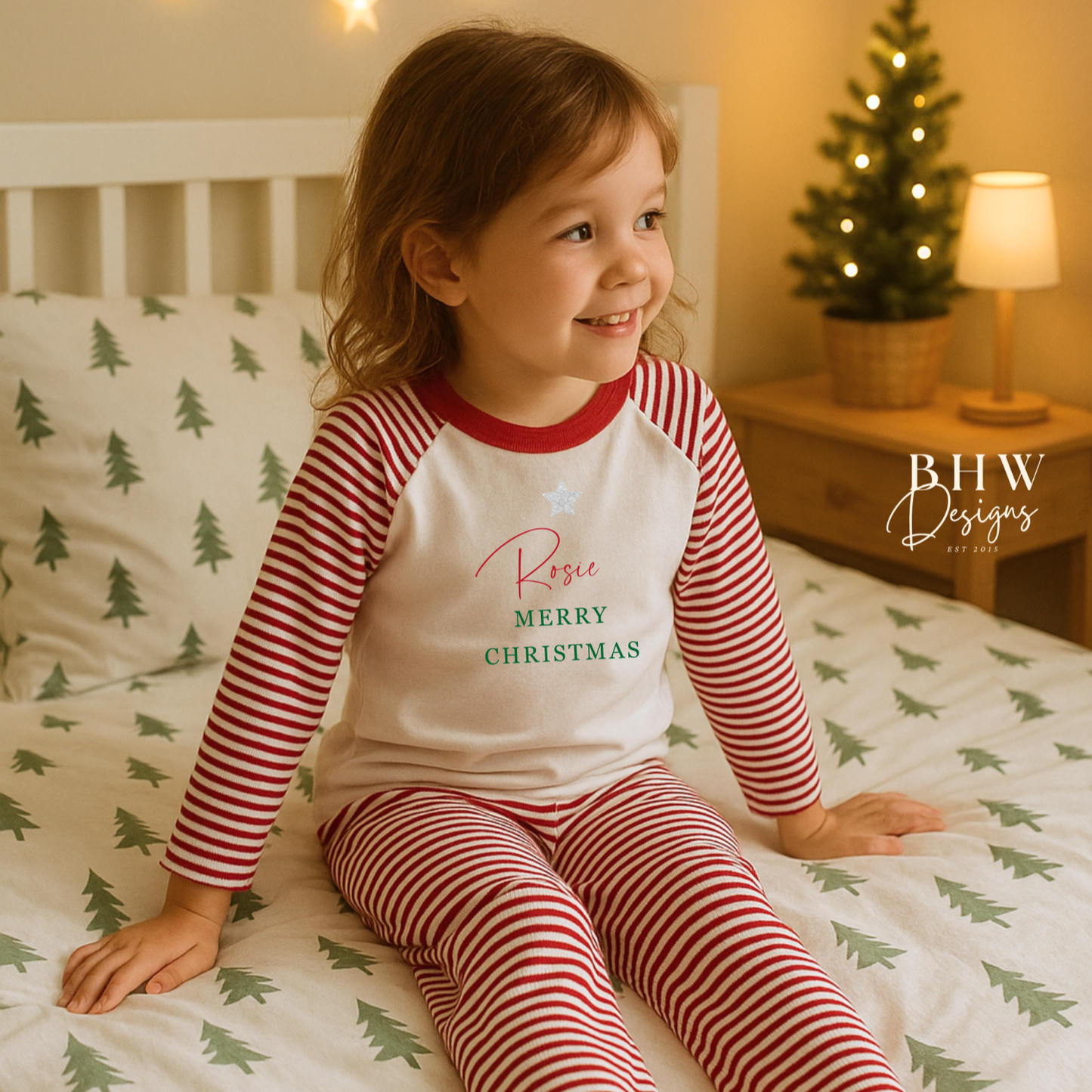 Child wearing red and white striped pyjamas with Rosie and 'Merry Christmas' text, sitting on a bed with Christmas tree patterns.